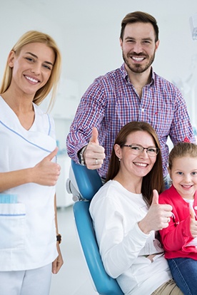 Mother father and child giving thumbs up in dental treatment room with dental team member